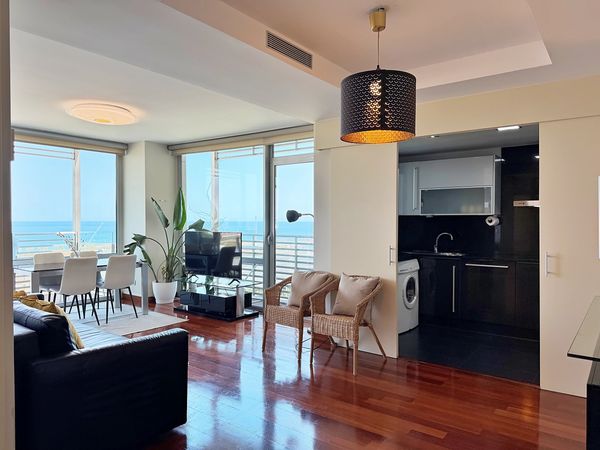Modern living room with ocean view, wooden floor, and open kitchen.
