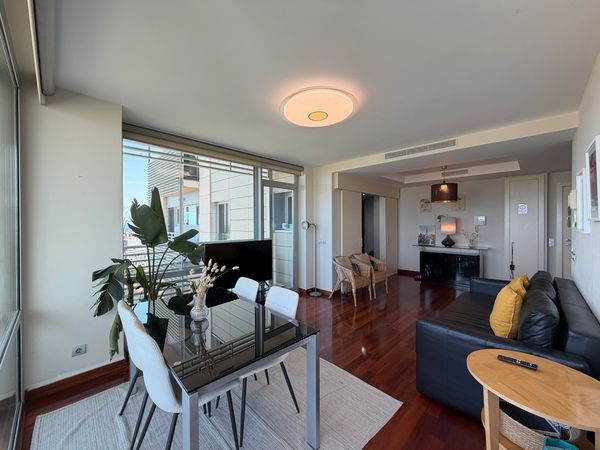 Modern living room with glass dining table, black leather sofa, and large window.