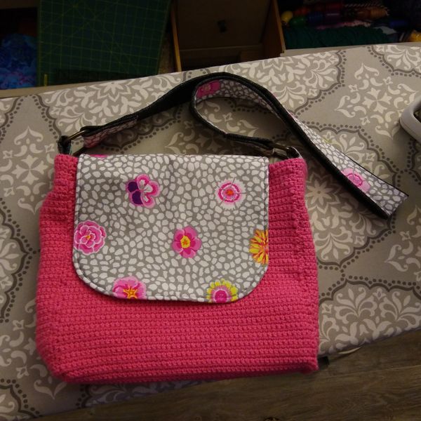 pink purse with colorful flap and cross-body strap on a gray ironing board.