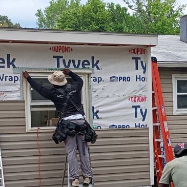 Worker installing window frame on house under construction.
