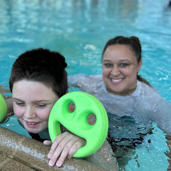 Child and adult smiling in pool with green floaties.