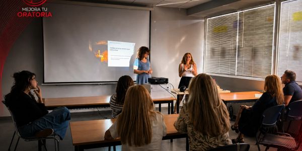 Two women giving a presentation to a small audience in a classroom setting.
