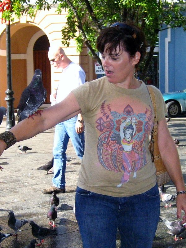 Woman surprised by pigeons landing on her arm in a city square.