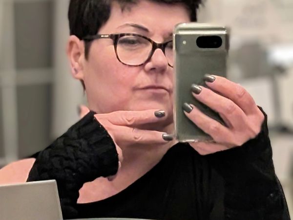 Woman taking a mirror selfie wearing glasses and black sleeves.