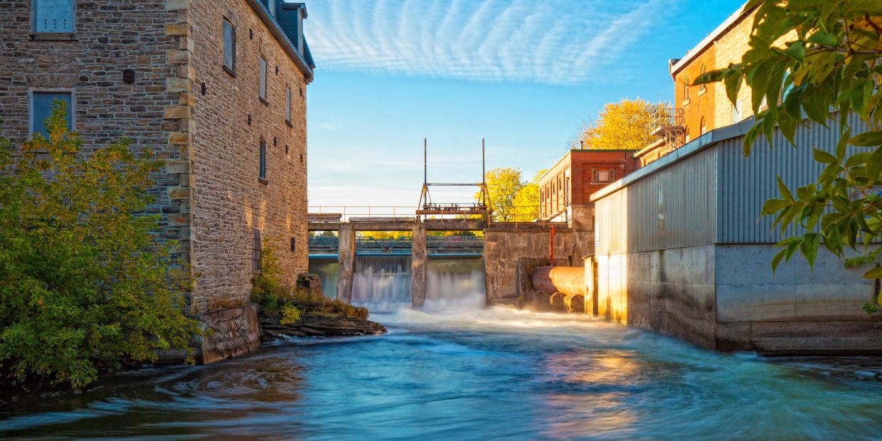 Water flowing through a dam near old buildings.