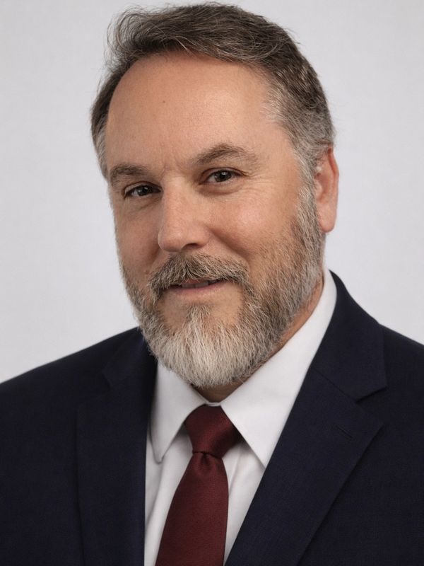 Portrait of a smiling man with a beard in a suit and tie.