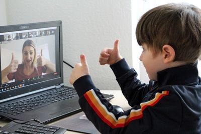 A child and woman giving thumbs up during a video call.