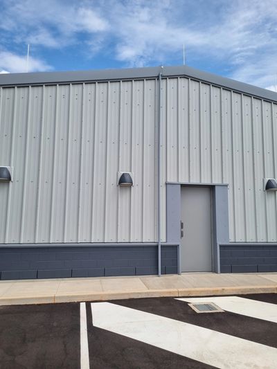 Gray industrial building with a metal door and striped pavement.