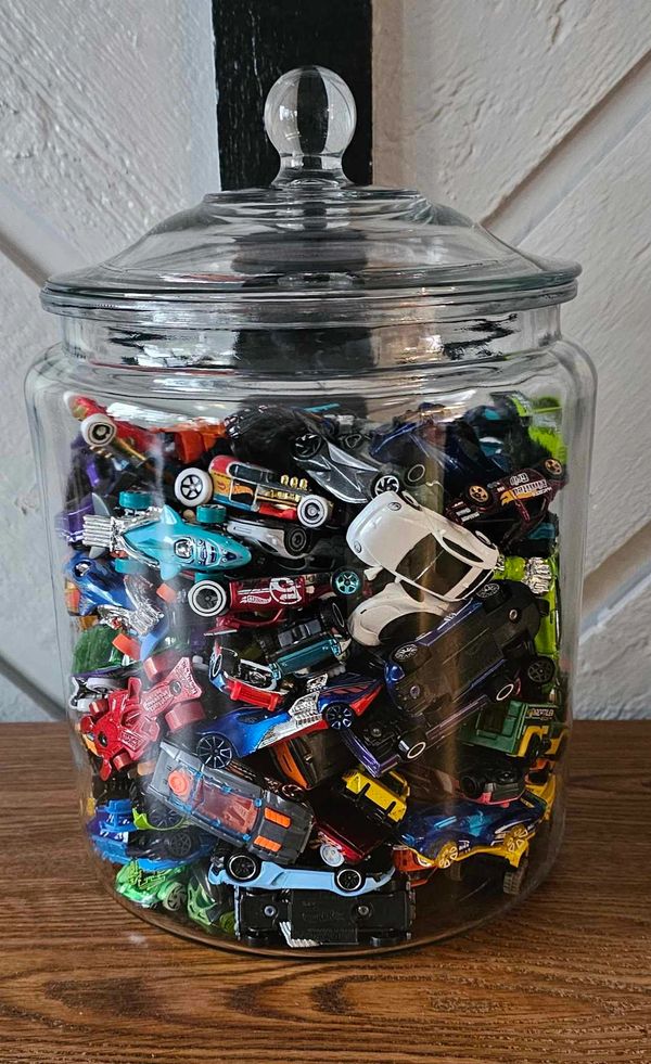 A glass jar filled with various colorful toy cars on a wooden surface.