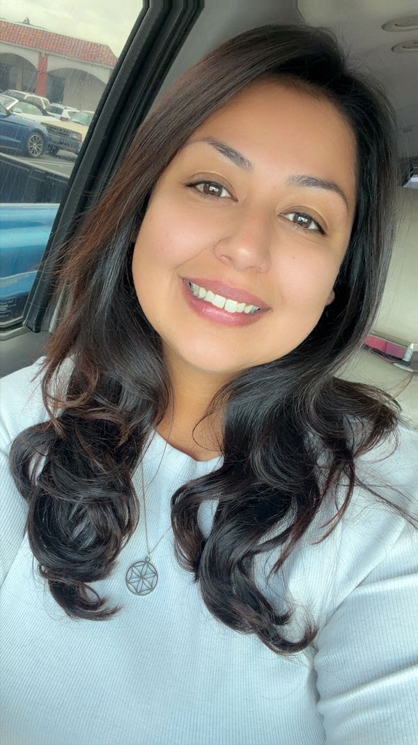 A woman with long dark hair smiling inside a car.