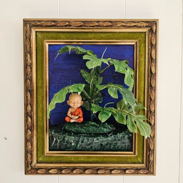 Framed 3D artwork of a meditating monk amidst lush green leaves.