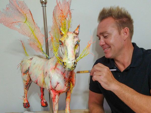 Artist painting a unique unicorn sculpture with vibrant colors and delicate wings.