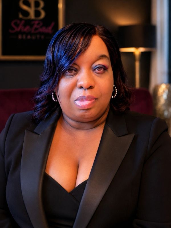 Confident woman in black blazer posing indoors.