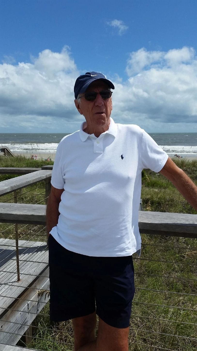 Elderly man in white polo and navy shorts at a beach boardwalk.