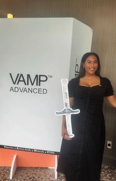 Woman standing beside a large VAMP Advanced display, holding a giant syringe prop.