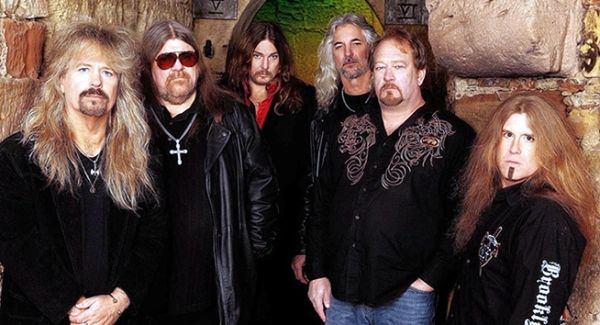 Group photo of six men with long hair and dark clothing.