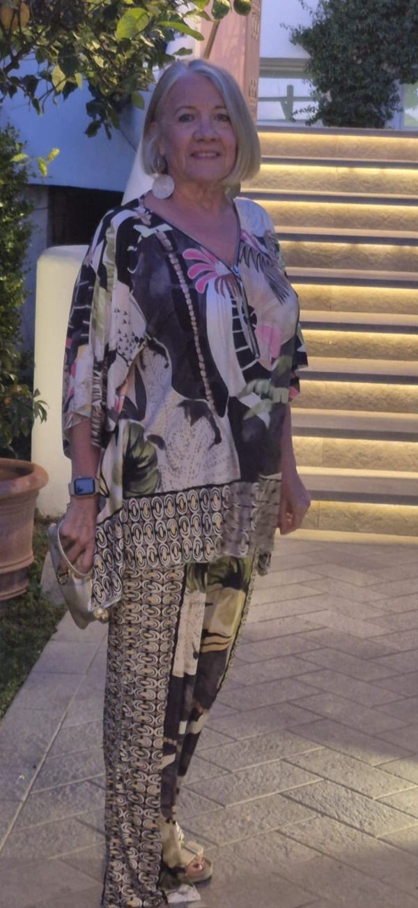 Older woman in colorful patterned outfit standing near lit stairs.