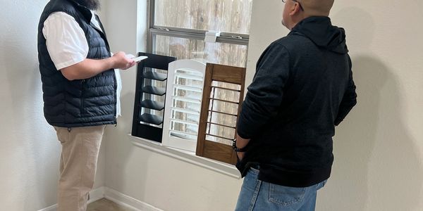 Two men examining window shutter samples held in a window frame.