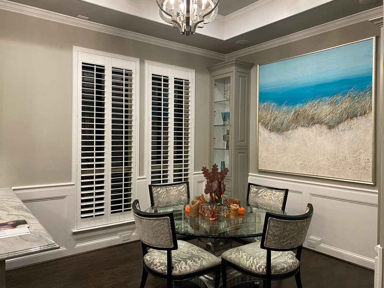 Elegant dining area with glass table, cushioned chairs, and large coastal painting.