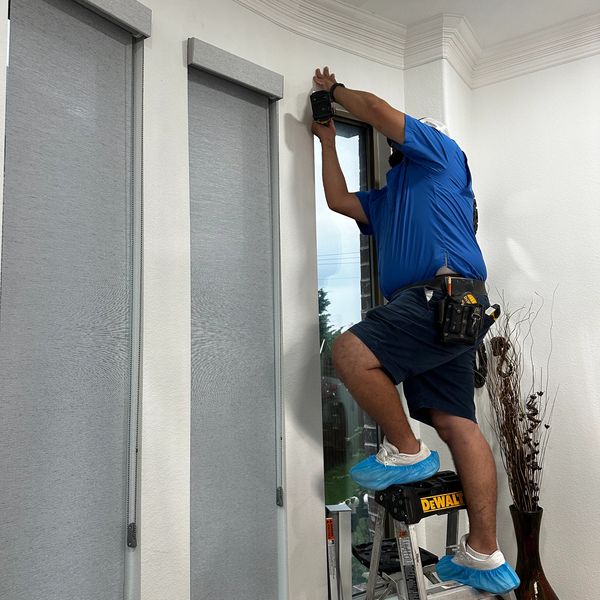Worker installing or repairing a window blind while standing on a ladder.