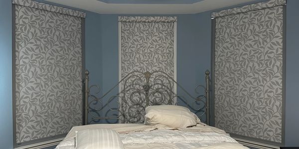Elegant bedroom with ornate iron bed and patterned window shades.