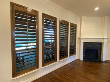 Four wooden shuttered windows next to a fireplace in a room with hardwood floors.