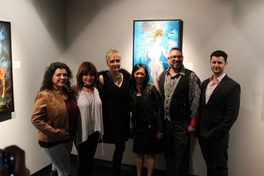 A group of six people posing in an art gallery with vibrant paintings.