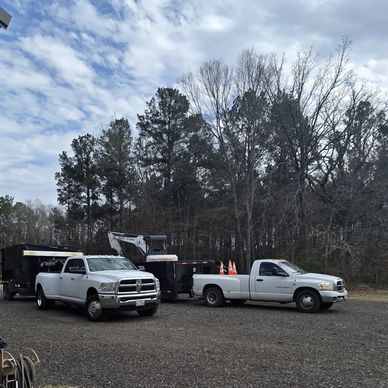 Two white pickup trucks parked with forest background.
