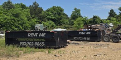 Two rental dumpsters with contact number in a yard.