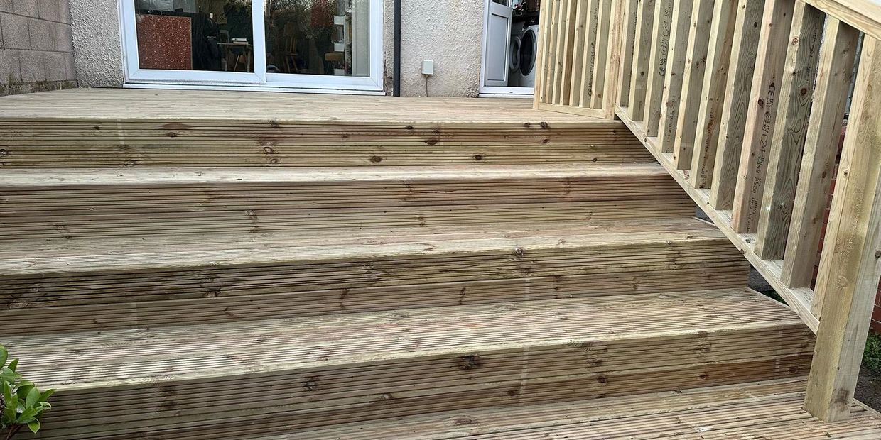 Newly built wooden deck stairs with a handrail leading to a sliding glass door 