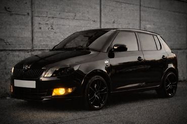 Sleek black car with glowing amber fog lights parked by a concrete wall.