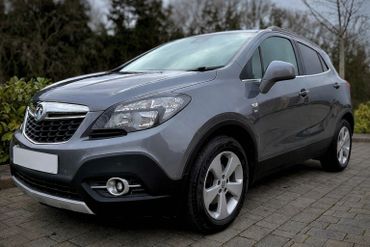 A sleek grey compact SUV parked on a driveway with trees in the background.