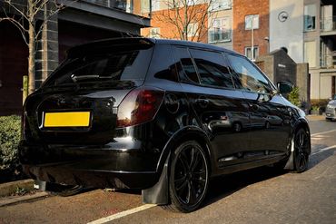 Black hatchback car parked on a city street under sunlight.