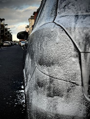 Close-up of a car covered in soap suds during a wash.