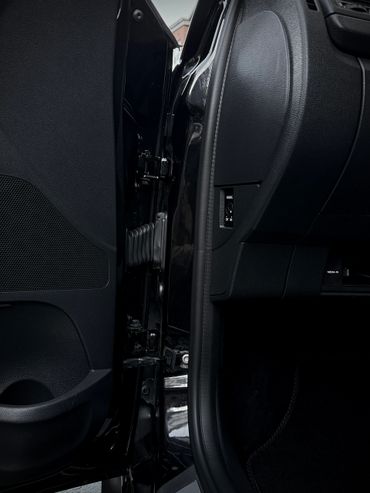 Close-up of a car door hinge area with black interior panels.