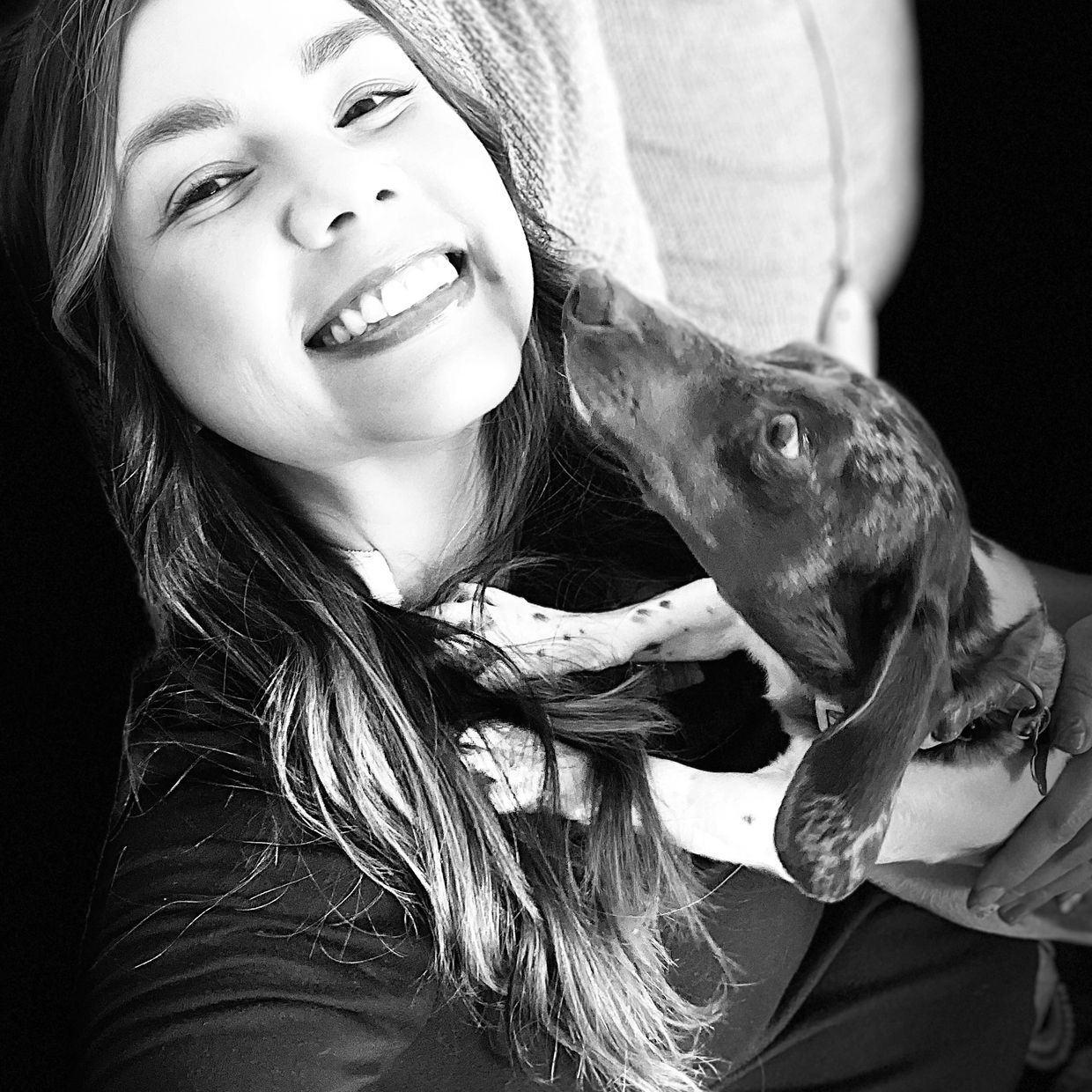 Young woman smiling as a dog licks her face in a black-and-white photo.
