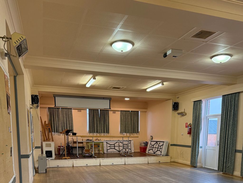 Empty community hall with a small stage and covered windows.
