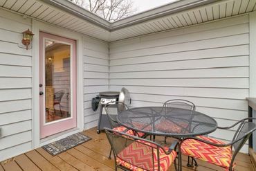 Cozy outdoor patio with a round metal table, colorful cushioned chairs, and a small grill.