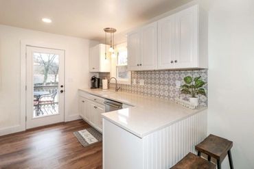 Bright kitchen with white cabinets, patterned backsplash, and wooden stools.