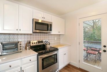 Modern kitchen with white cabinets, stainless steel appliances, and a door leading to an outdoor deck.