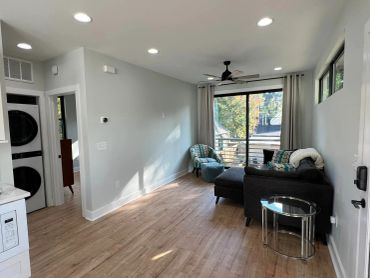 Cozy living room with a dark sectional sofa, patterned chair, and large window.