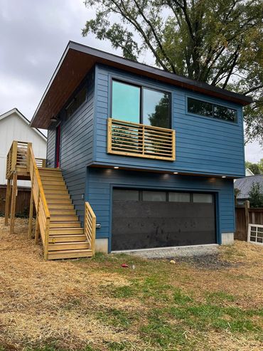 Modern two-story blue house with wooden stairs and balcony railing.