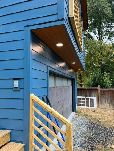 Modern blue house exterior with wooden railing and recessed lighting.
