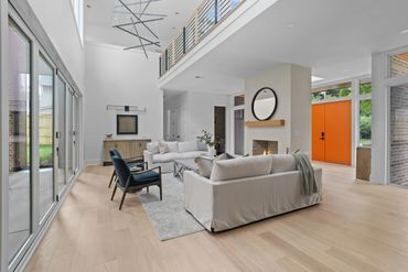 Modern living room with white sofas, blue chairs, and an orange front door.
