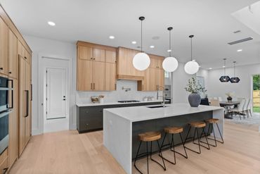 Modern kitchen with wooden cabinets, white marble island, and spherical pendant lights.