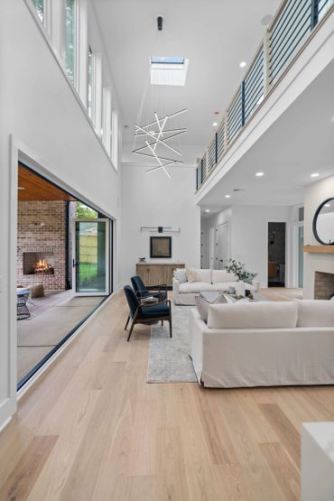 Modern living room with high ceilings, light wood floors, and large sliding doors to an outdoor fireplace.