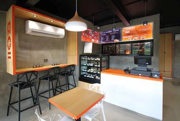 Modern cafe interior with orange and black accents, bar stools, and a display counter.
