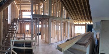 Interior view of a house under construction with wooden framing and stairs.