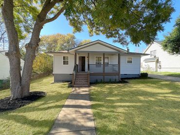 Small white house with a porch and large tree in front yard.