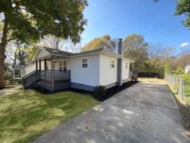 Cozy white house with a small porch and a spacious driveway on a sunny day.